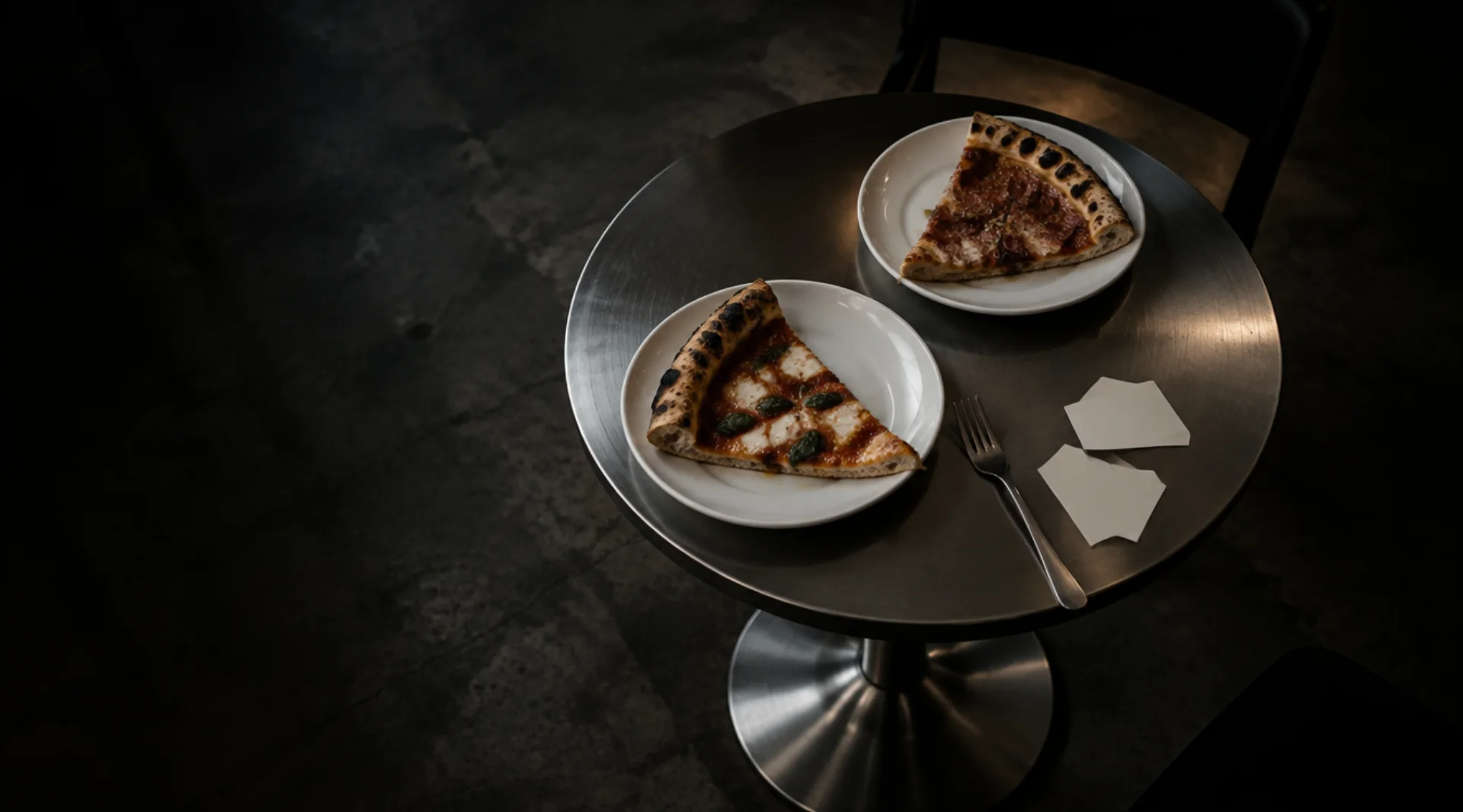 Två pizzabitar på tallrikar från Fornello, på ett sidobord i stål
